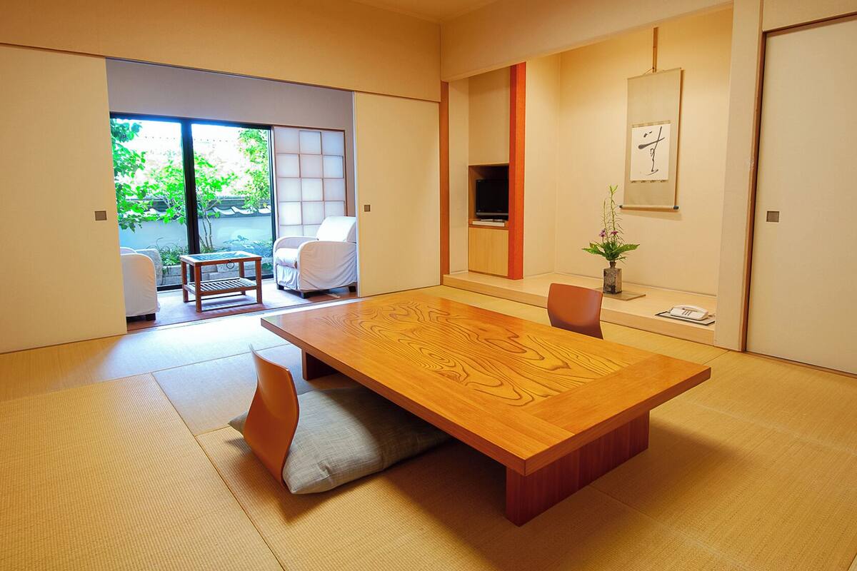 Une pièce de style japonais traditionnel, avec un sol recouvert de tatamis, une petite table en bois et une porte coulissante donnant sur un balcon.