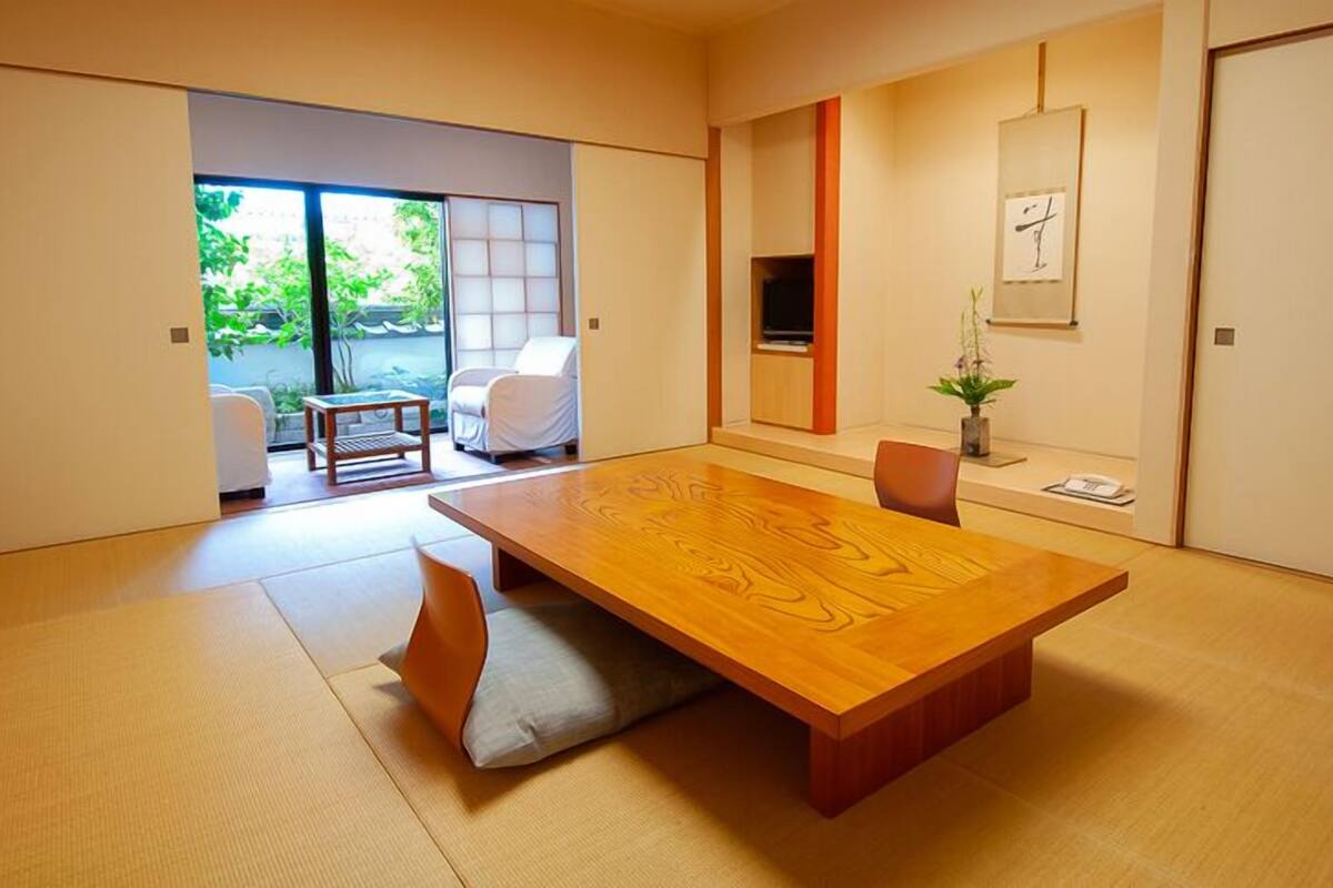 Une pièce de style japonais traditionnel, avec un sol recouvert de tatamis, une petite table en bois et une porte coulissante donnant sur un espace extérieur.