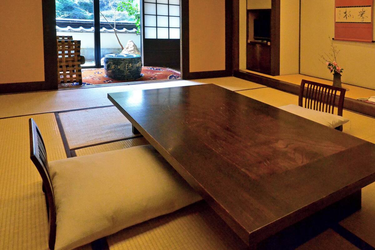 Une pièce de style japonais traditionnel, avec un sol recouvert de tatamis, une petite table basse en bois, un paravent shoji et un petit bonsaï.