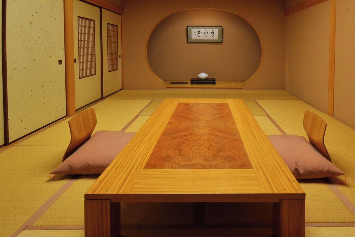Une pièce au sol recouvert de tatamis, avec une petite table basse, des coussins et un paravent en papier de riz (shoji).