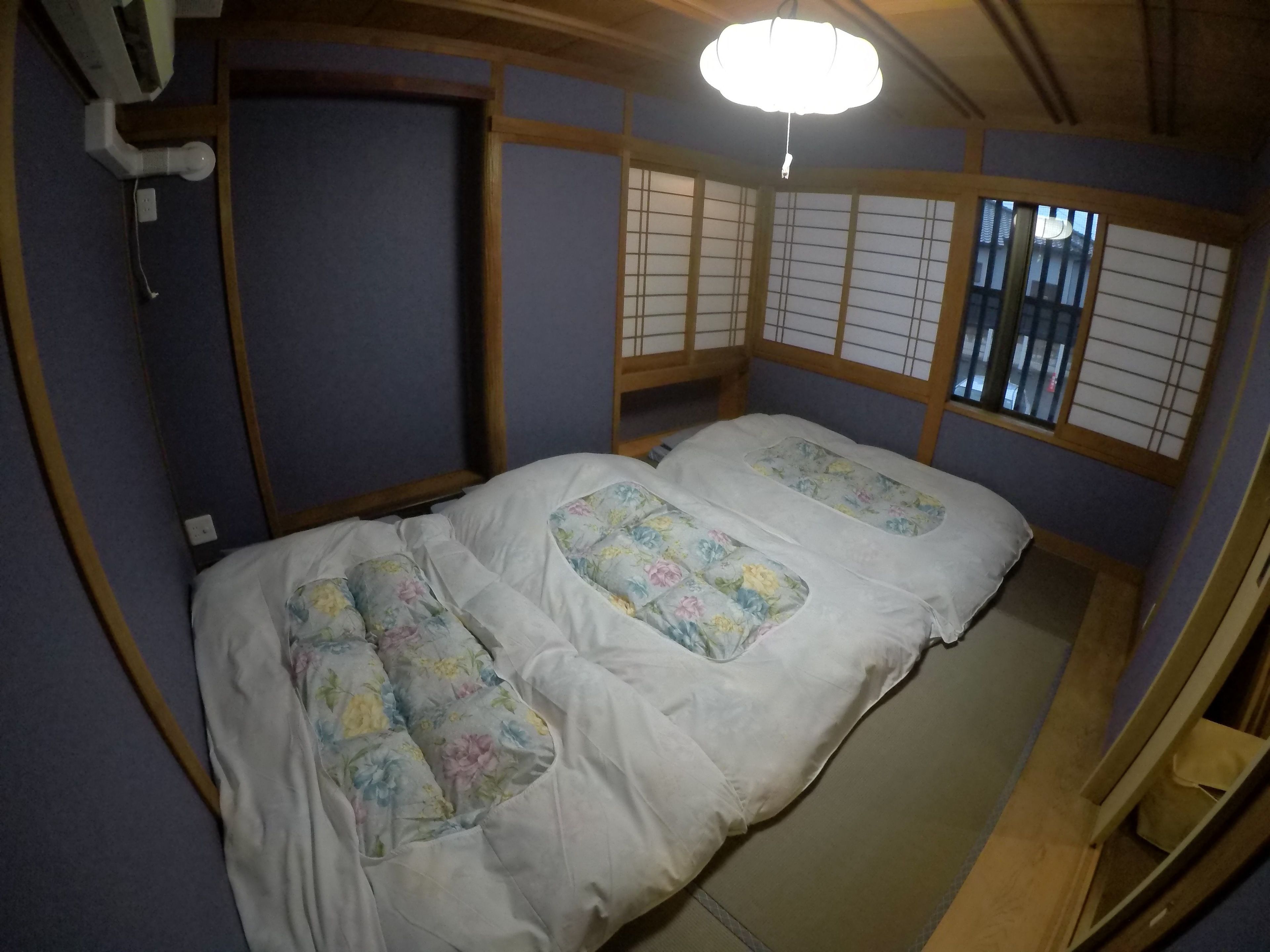 Um quarto japonês tradicional, com piso de tatame, uma cama de madeira baixa com roupa de cama florida e biombos shoji.