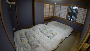 Um quarto japonês tradicional, com piso de tatame, uma cama de madeira baixa com roupa de cama florida e biombos shoji.