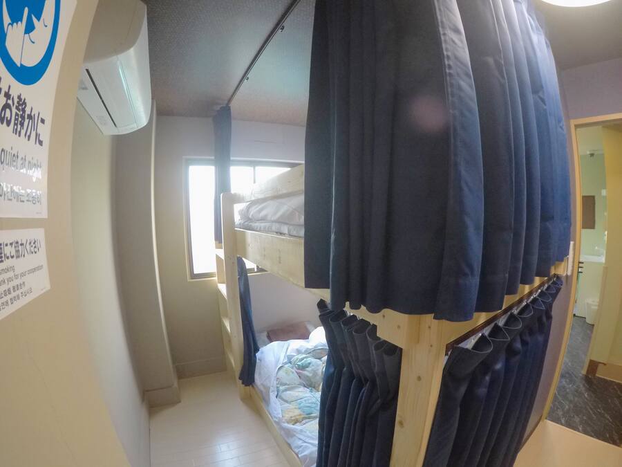 A dormitory room with bunk beds, a window, and a curtain rod with multiple curtains.