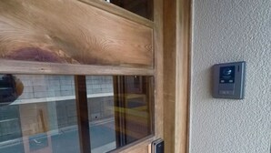 A wooden door with a glass panel, a metal handle, and a Panasonic security device mounted on the wall.