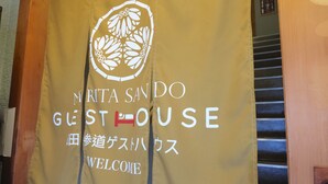 A yellow welcome banner with the text "MIRTA SANDO GUEST HOUSE" and Japanese characters.