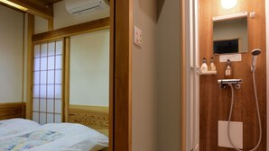 A traditional Japanese-style room with a wooden bed, sliding shoji doors, and a wooden washbasin with a mirror and soap bottles.
