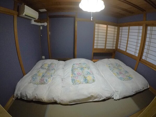 Une pièce de style japonais traditionnel, avec un sol recouvert de tatamis, un futon avec une literie à motifs floraux, des paravents shoji et un ventilateur de plafond.