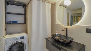 A compact bathroom with a washing machine, a sink with a modern design, and a mirror with a circular light.