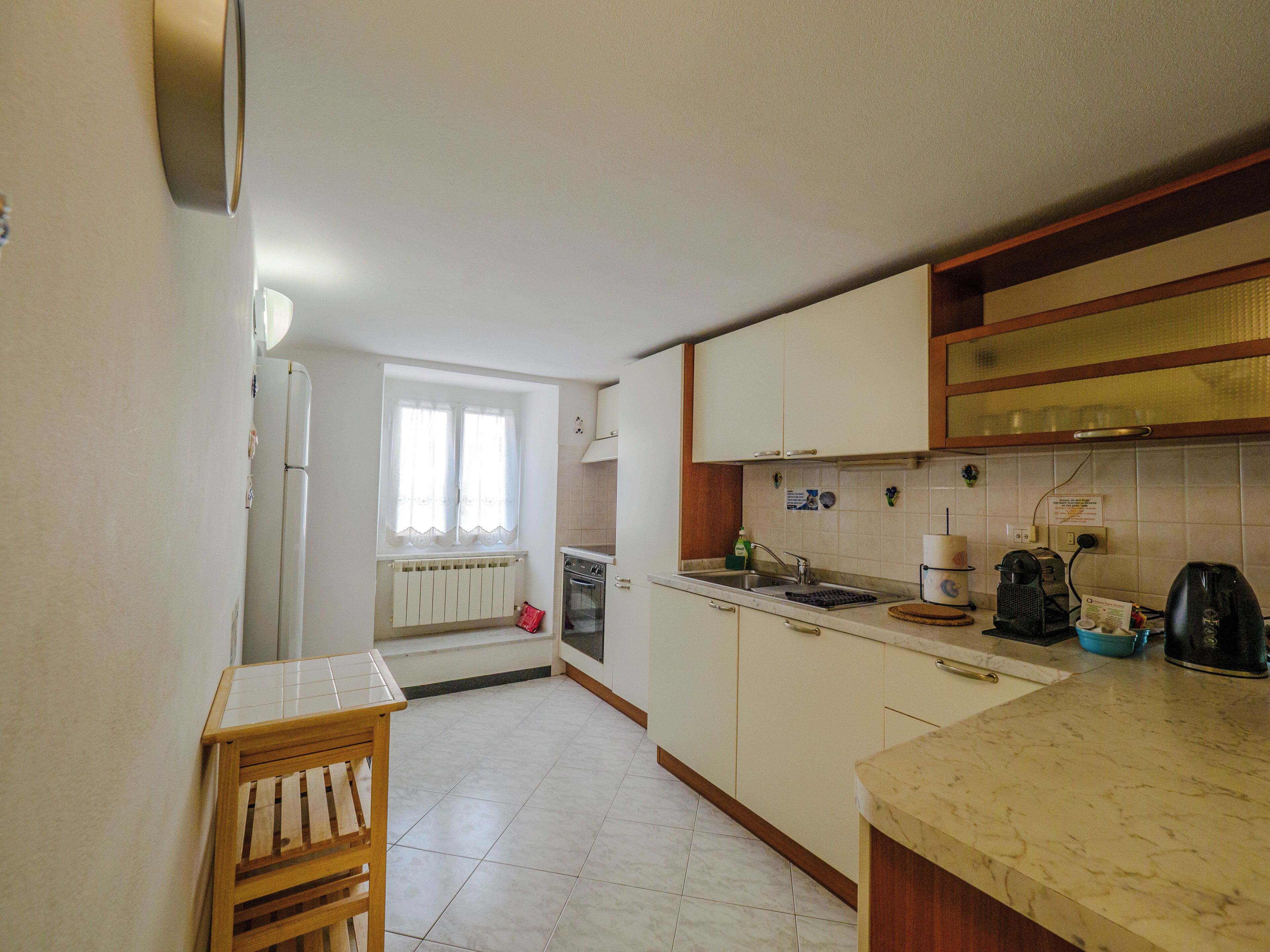 Cucina con mobili bianchi, un tavolo di legno e una finestra con tende.