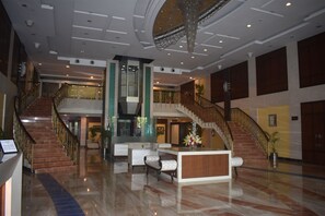 Eine großzügige Lobby mit einer imposanten Treppe, einem Empfangstresen und einer Sitzecke.