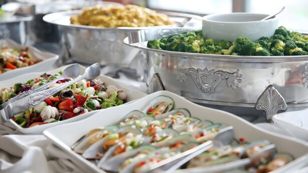 Een buffet met diverse gerechten, waaronder een grote kom broccoli, een salade en ander gevarieerd eten.