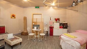 Habitación de hotel con cama, una pequeña mesa con sillas, kitchenette y una zona de estar con ventilador.