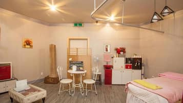 Habitación de hotel con cama, una pequeña mesa con sillas, kitchenette y una zona de estar con ventilador.