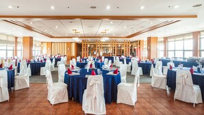 Un amplio salón de banquetes con mesas redondas cubiertas con manteles azules y sillas blancas con cintas blancas.
