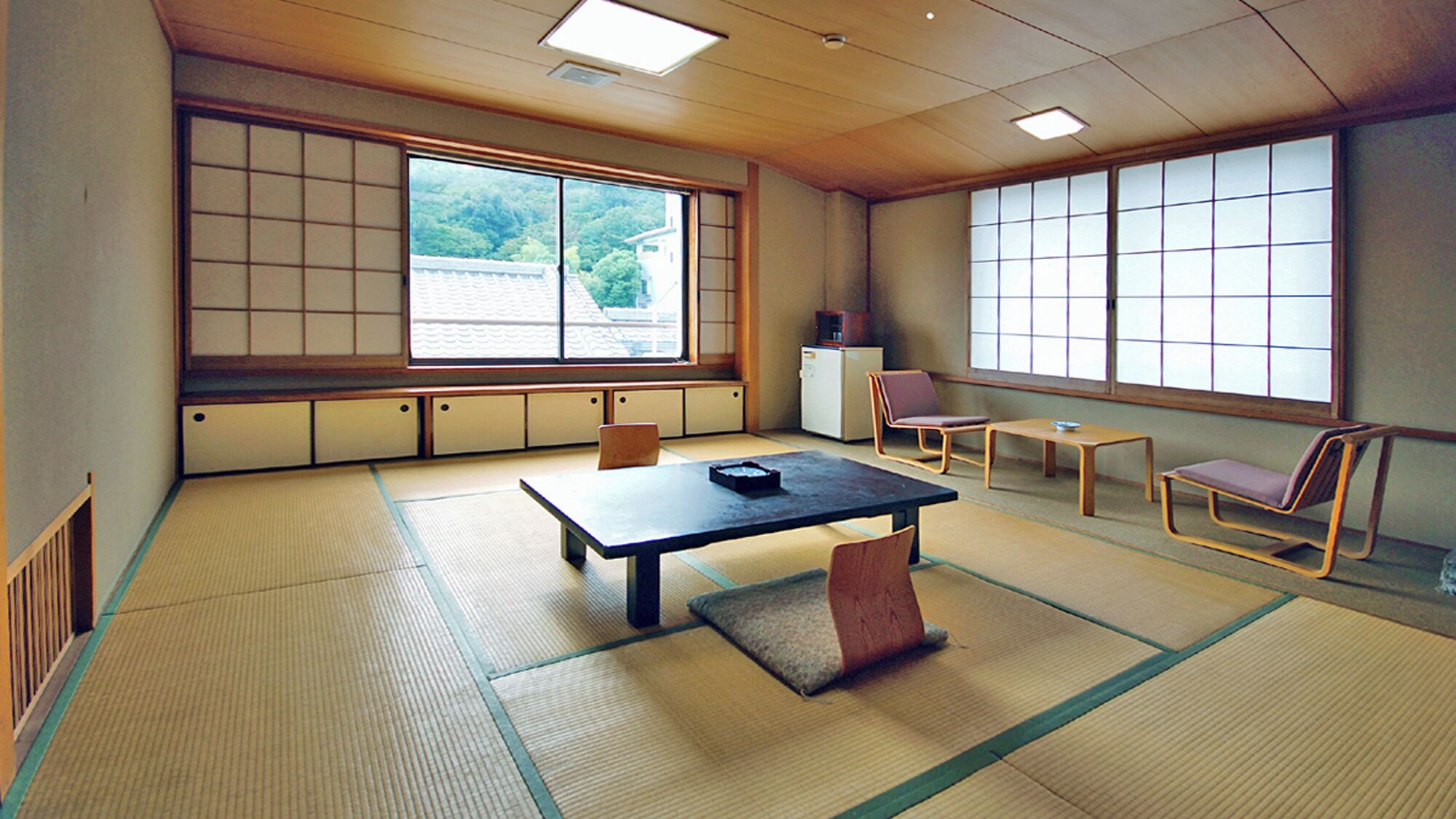 A traditional tatami mat room with a low table, chairs, and large windows.