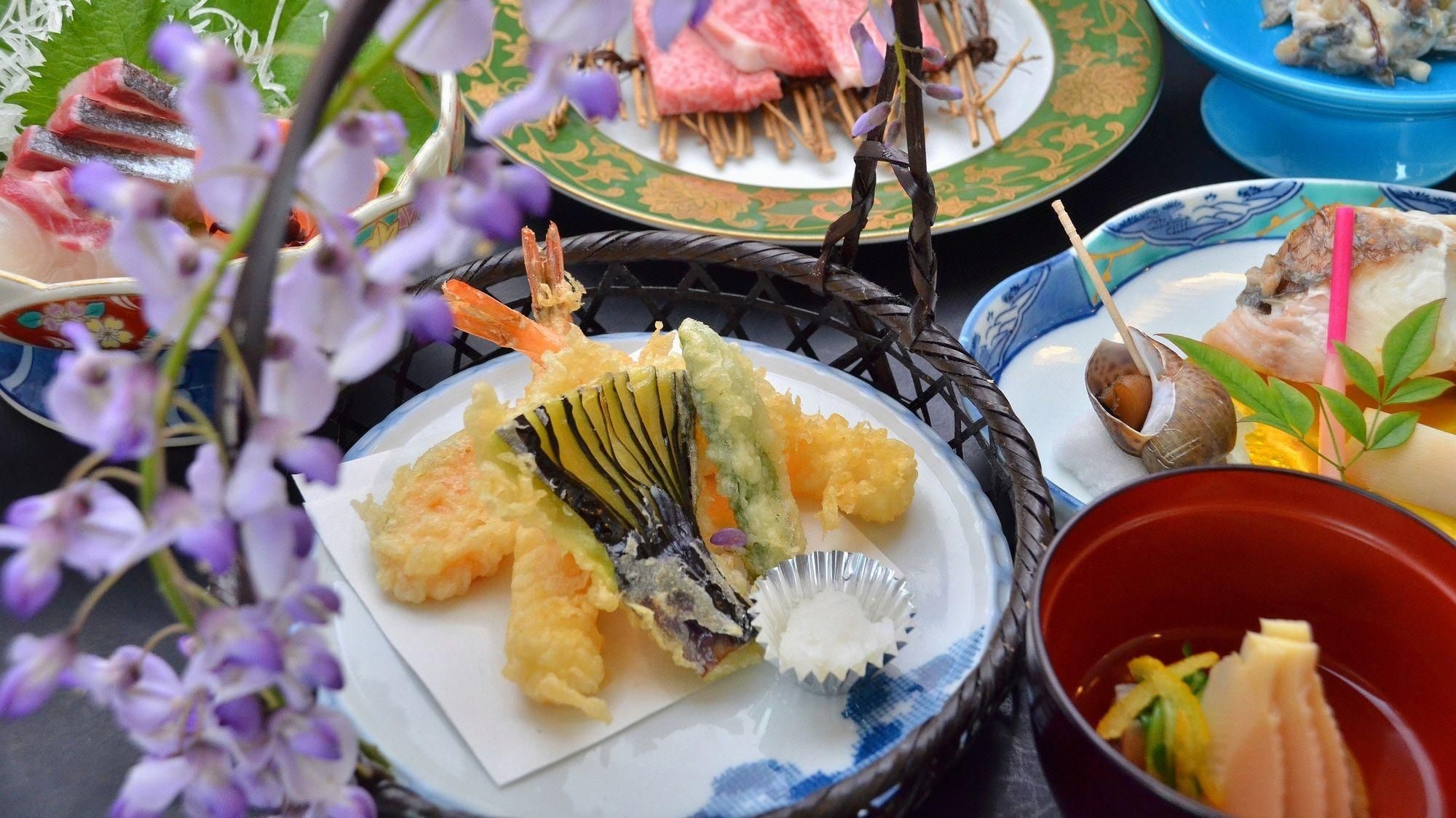 A variety of Japanese dishes, including tempura and sashimi, arranged on a table with floral decorations.