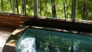 Piscina com interior em azulejo, rodeada por um muro de tijolos e grandes janelas que oferecem vista para uma floresta verde exuberante.