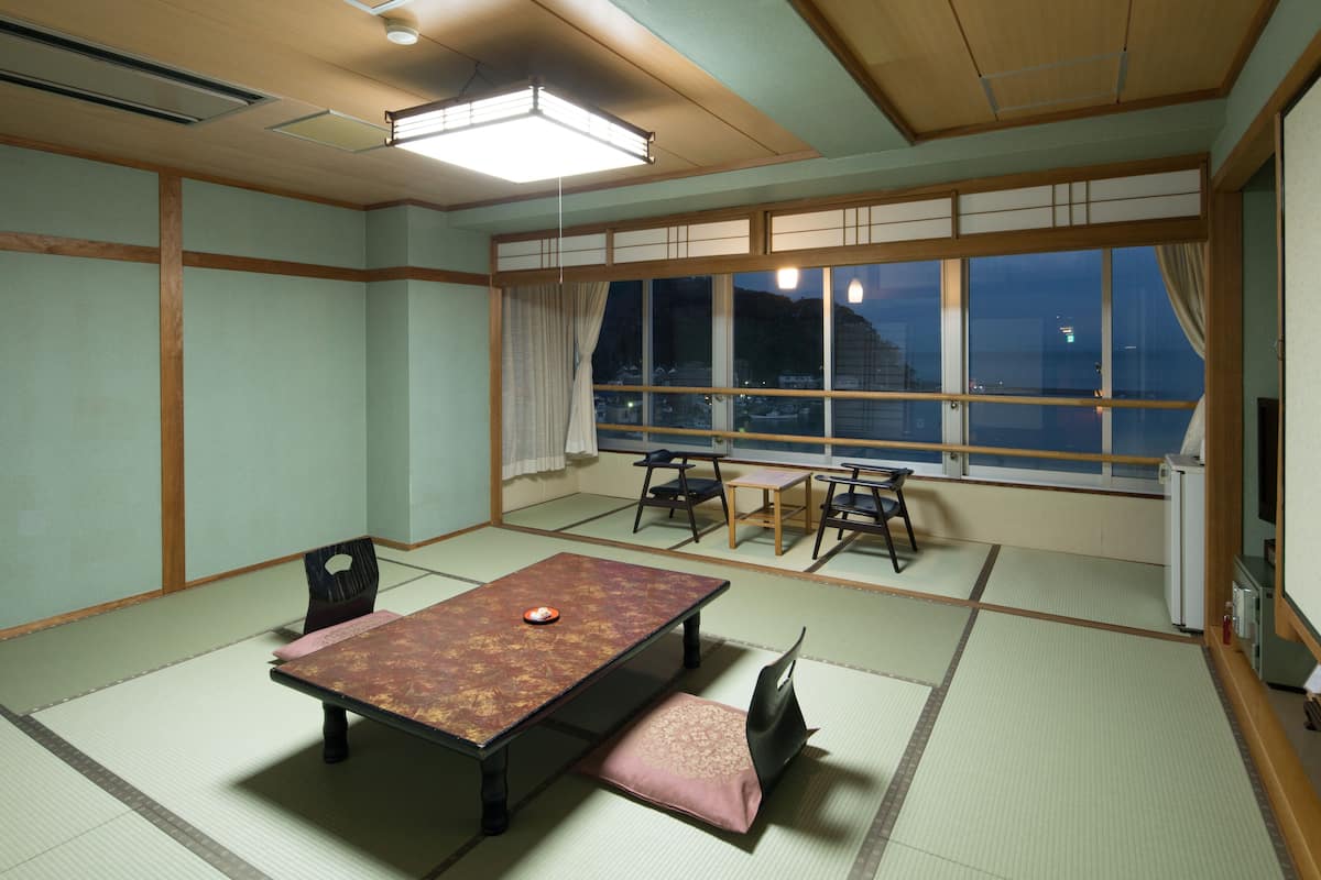 Ein traditioneller japanischer Raum mit Tatami-Böden, einem niedrigen Tisch mit Kissen und Blick auf eine nächtliche Stadtansicht.