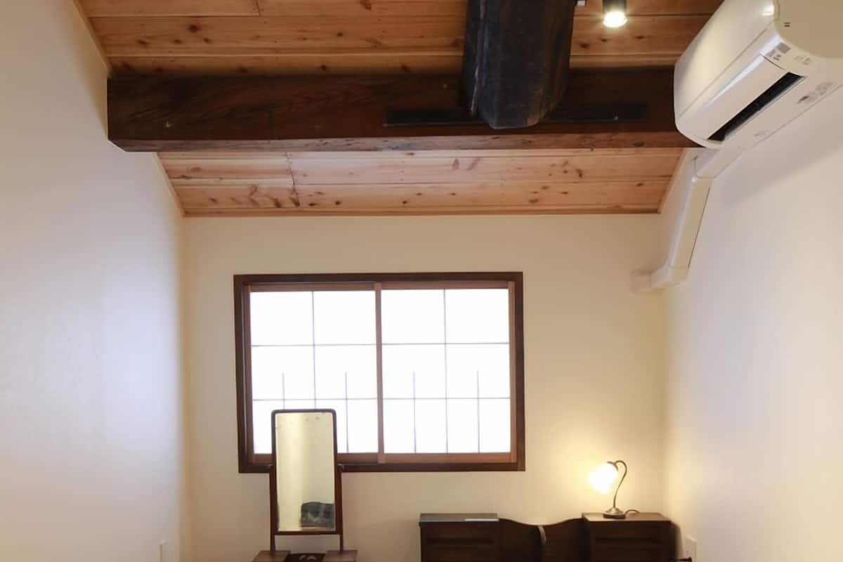 Ein traditioneller japanischer Raum mit Tatami-Bodenbelag, einem Shoji-Bildschirmfenster, einem kleinen Holzschrank und einem Deckenventilator.