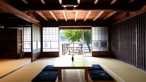 Une pièce de style japonais traditionnel, avec un sol recouvert de tatamis, une basse table en bois et des portes coulissantes donnant sur un espace extérieur avec vue sur les arbres et une table dressée pour deux personnes.