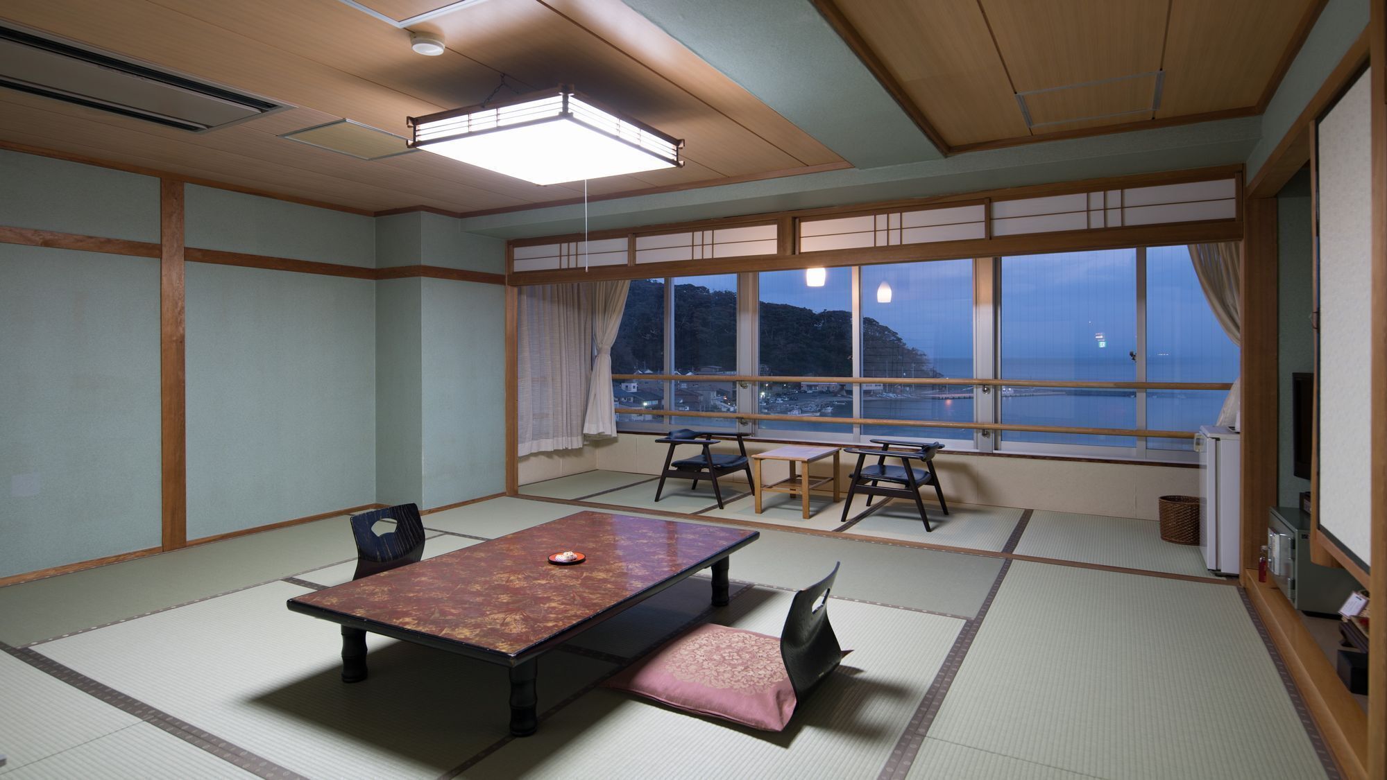 A traditional tatami room with a low table, chairs, and a view of the sea.