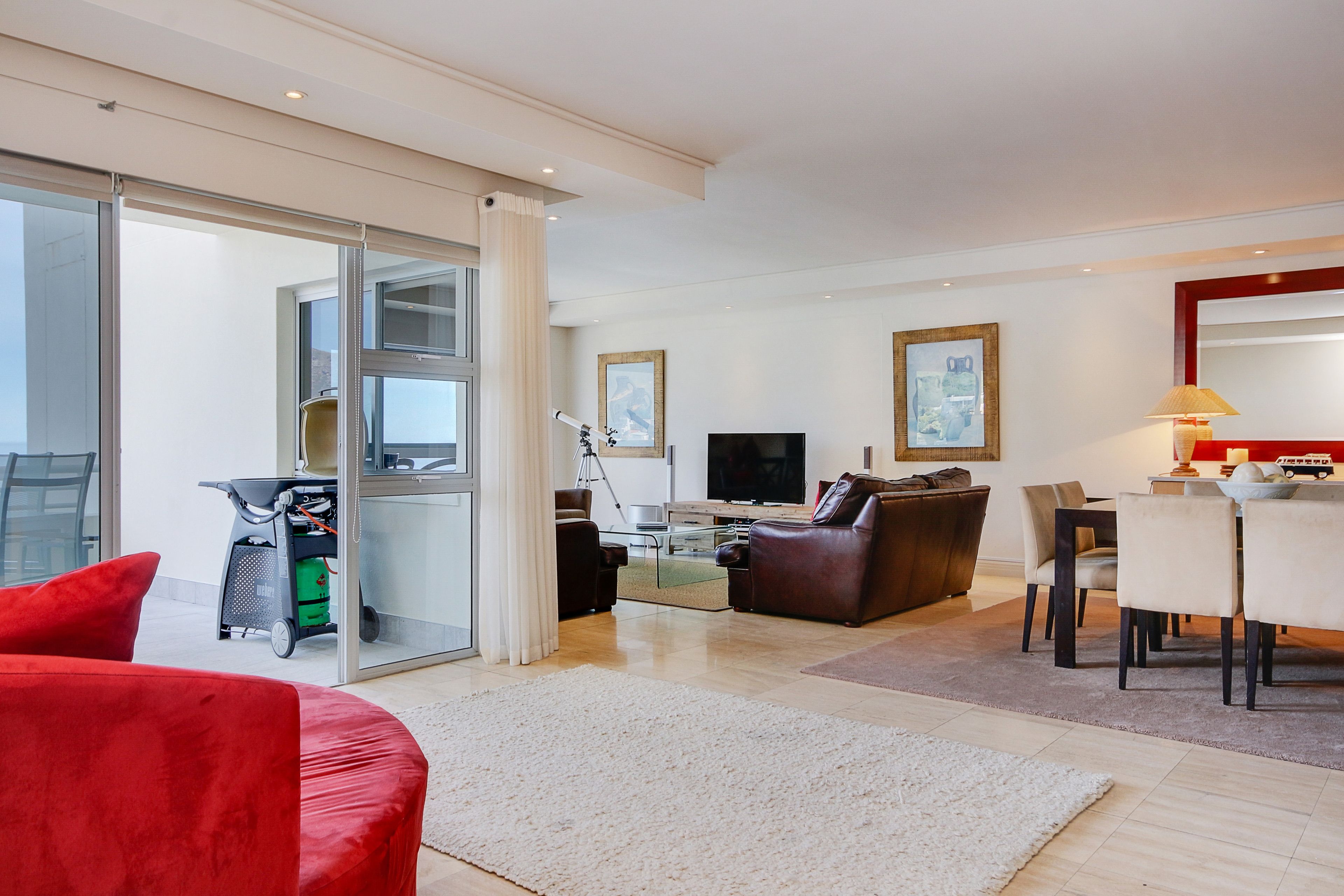 A modern living room with a sofa, a TV, a dining table, and a sliding glass door leading to a balcony.