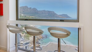 A room with a large window overlooking a coastal landscape, featuring two wicker chairs and a view of the sea and mountains. - Dunmore Views (Cape Town)