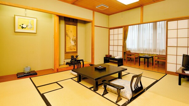 A traditional Japanese room with tatami flooring, a low table, chairs, a television, and artwork on the walls. - Hotel Matsuo (Hamada)