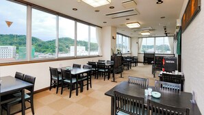 A spacious dining area with multiple tables and chairs, large windows offering a view of the city, and a Nescafé coffee machine on the right. - Hotel Matsuo (Hamada)