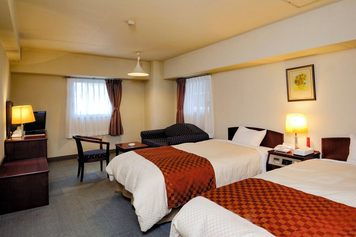 Habitación de hotel con dos camas, un escritorio, una silla y un televisor.