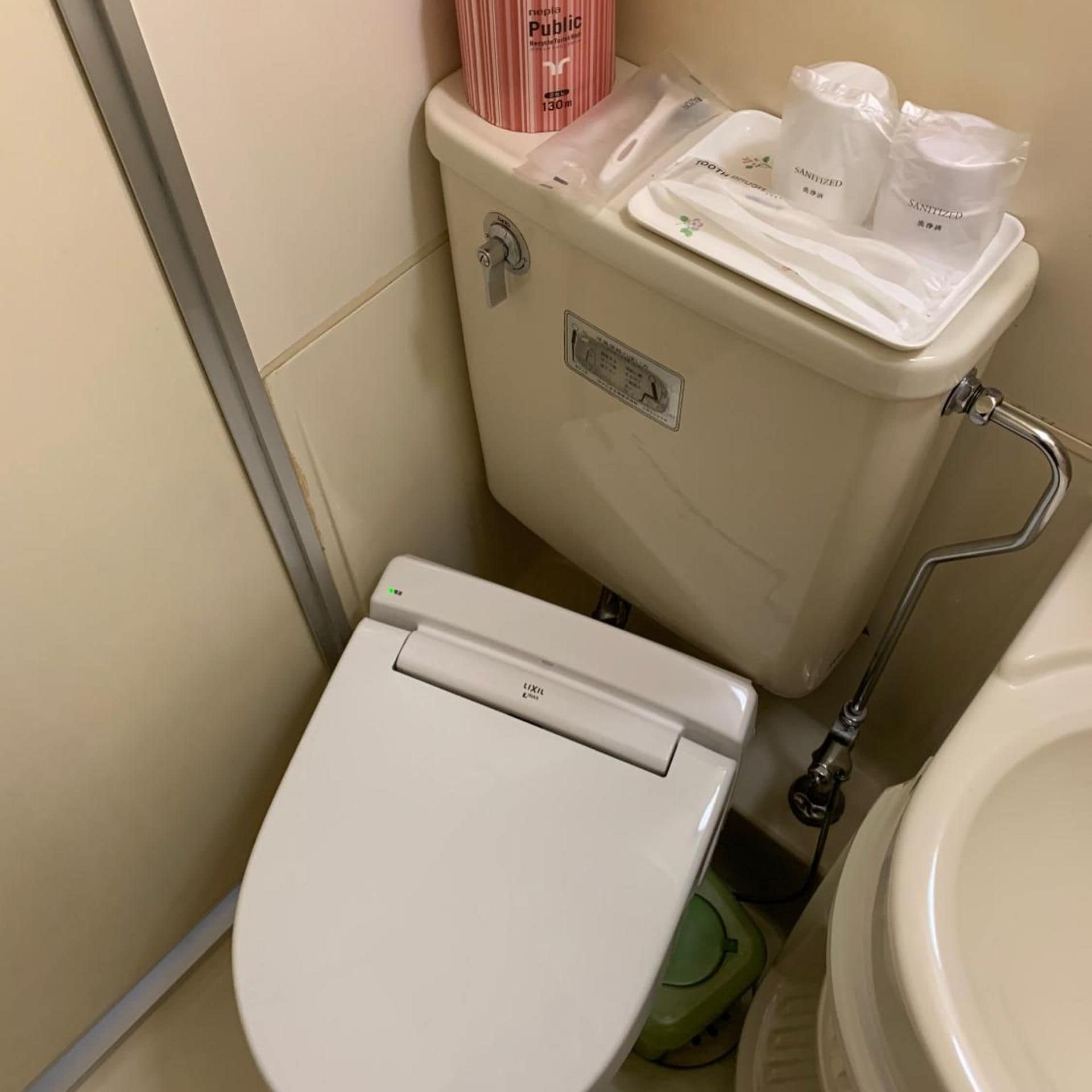 A toilet with a lid, a flush handle, and a bidet attachment.