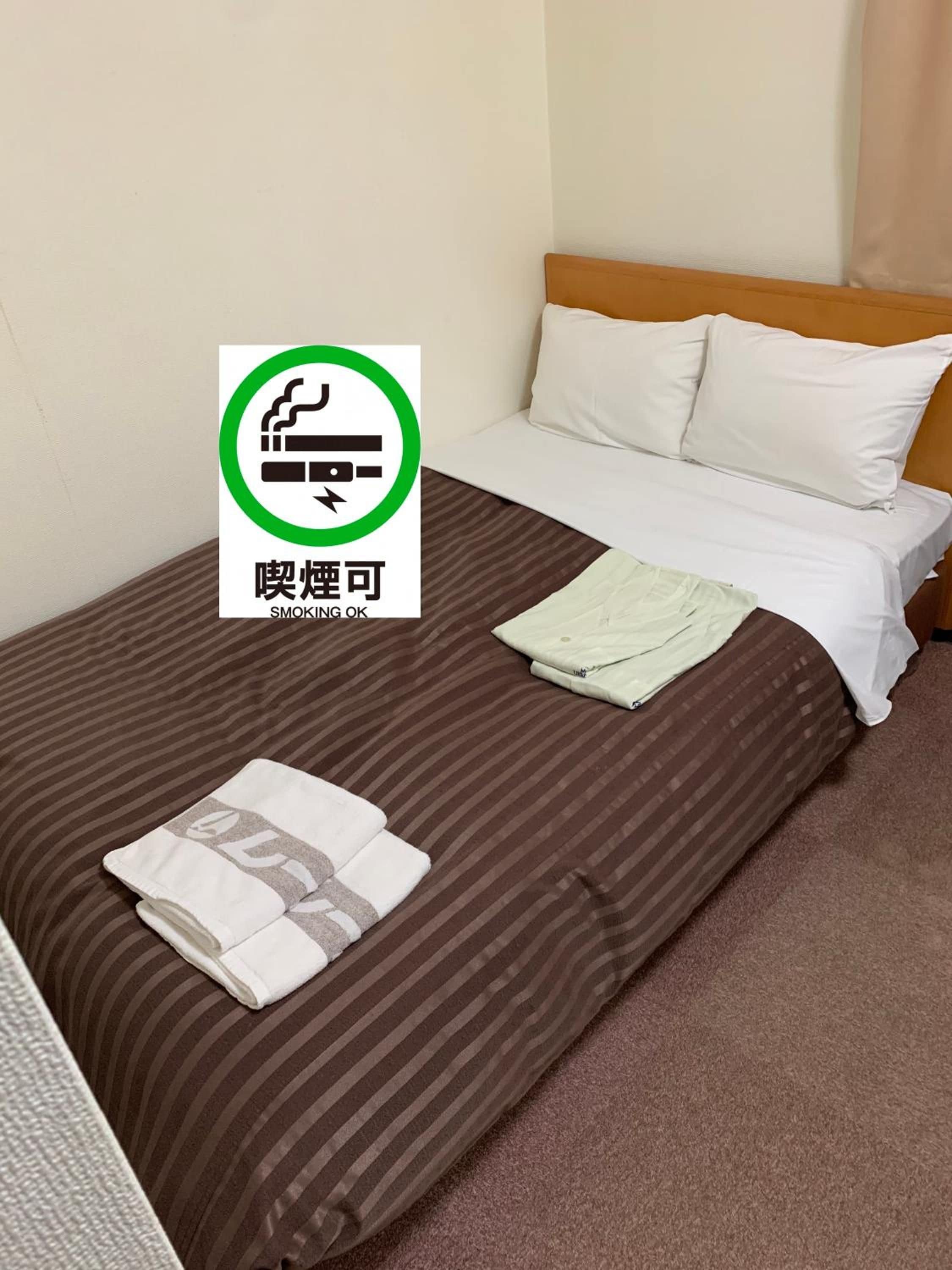 A hotel room with a bed, pillows, a folded towel, and a 'Smoking OK' sign.