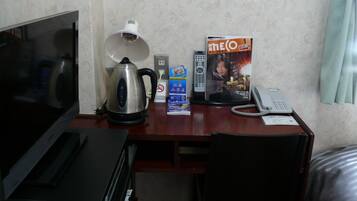 Ein Hotelzimmer mit Schreibtisch, Wasserkocher, Fernbedienung, Zeitschrift, Telefon und Fernseher.