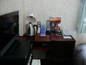 Habitación de hotel con escritorio, tetera, control remoto, revista, teléfono y televisor.