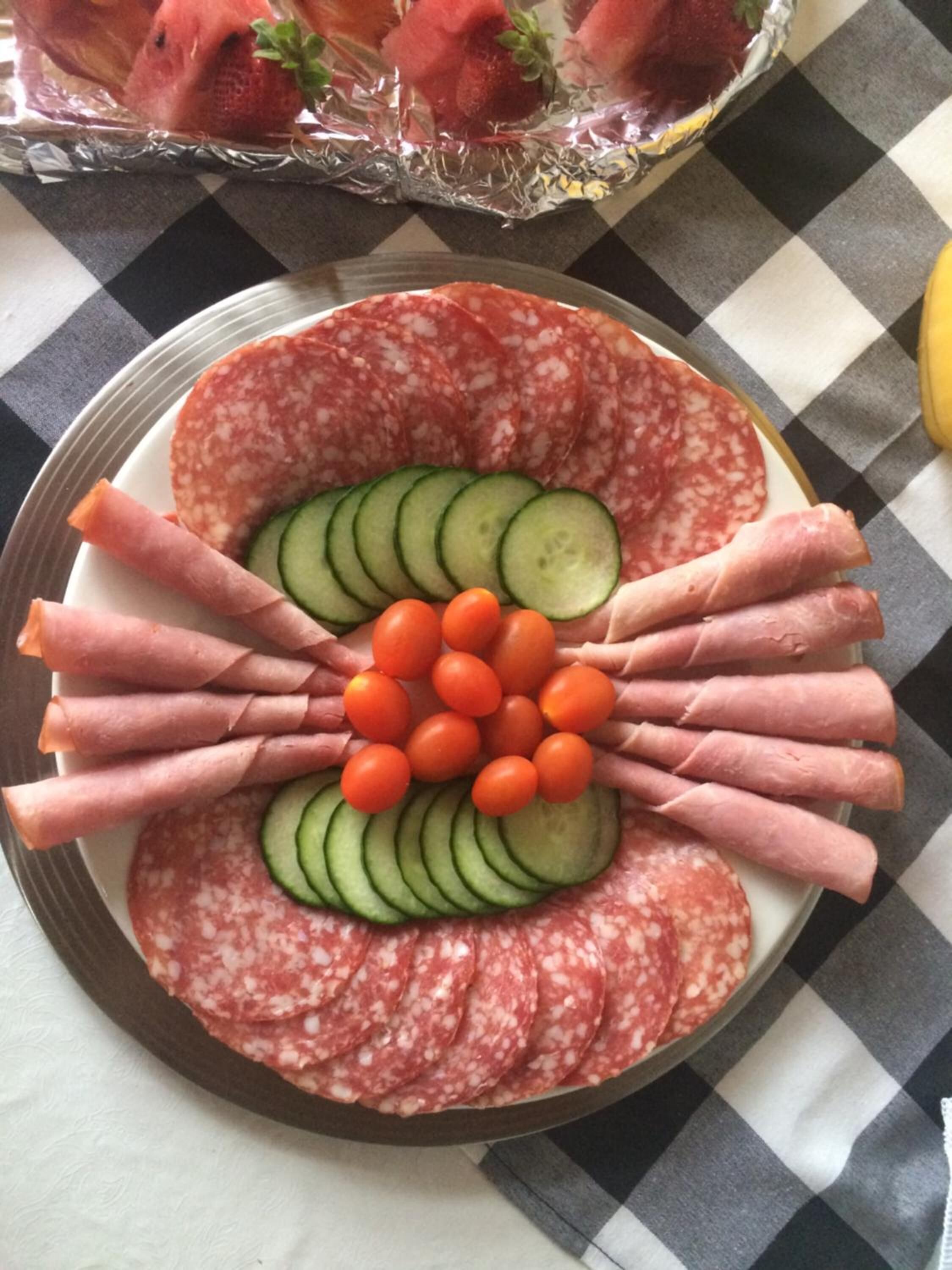 A charcuterie board with sliced salami, cucumber, cherry tomatoes, and prosciutto arranged on a plate.