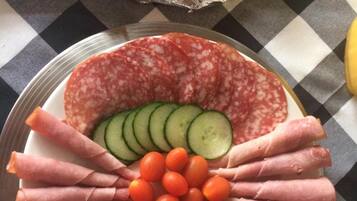 A charcuterie board with sliced salami, cucumber, cherry tomatoes, and prosciutto arranged on a plate.