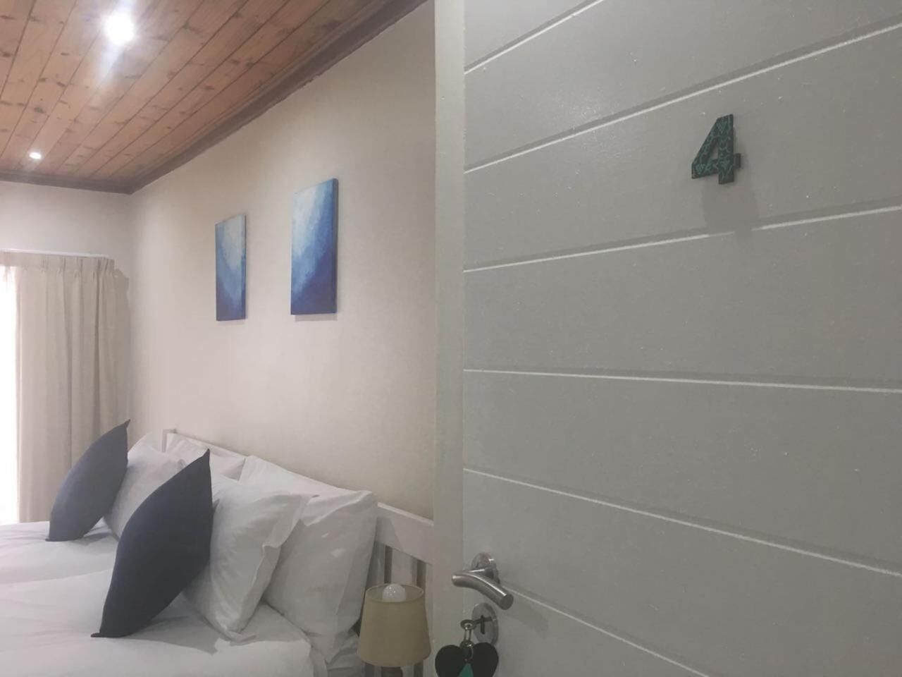 A hotel room with a bed, two pillows, a nightstand, a lamp, and a door with the number 4.