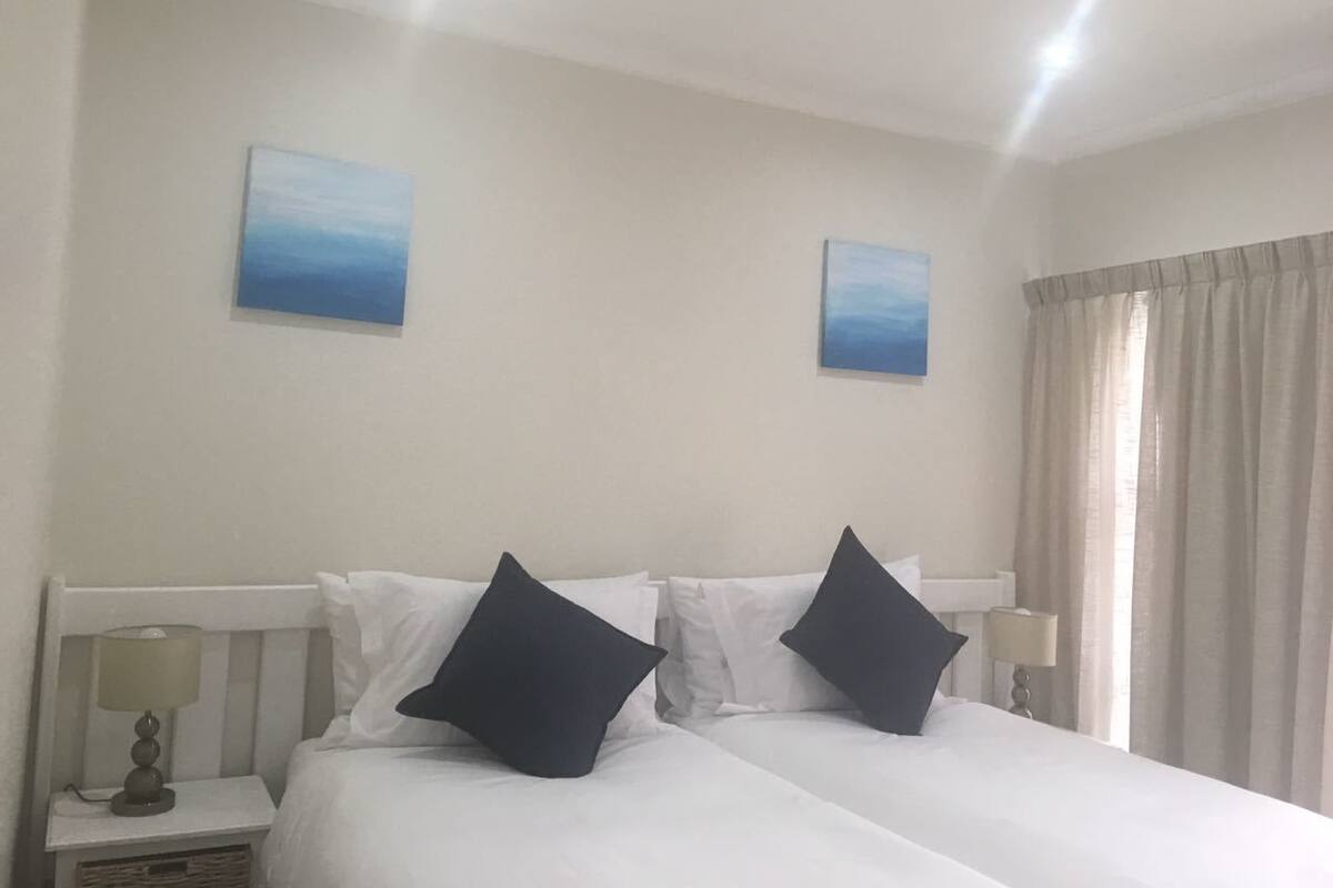 A hotel room with two beds, white bedding, and two blue paintings on the walls.