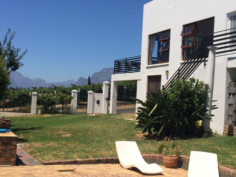 A swimming pool with two lounge chairs, a white building with a staircase, and a view of mountains in the background.