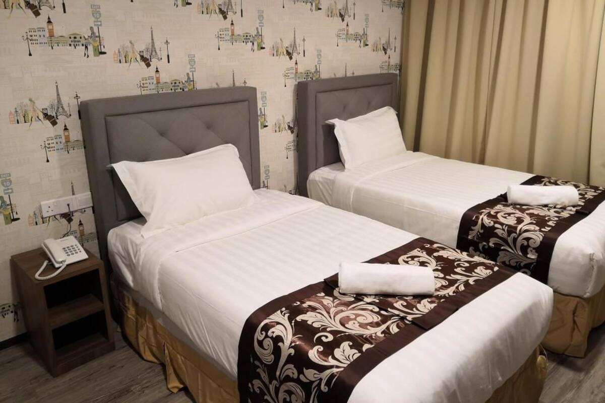 A hotel room with two beds, a nightstand with a phone, and a patterned wallpaper.