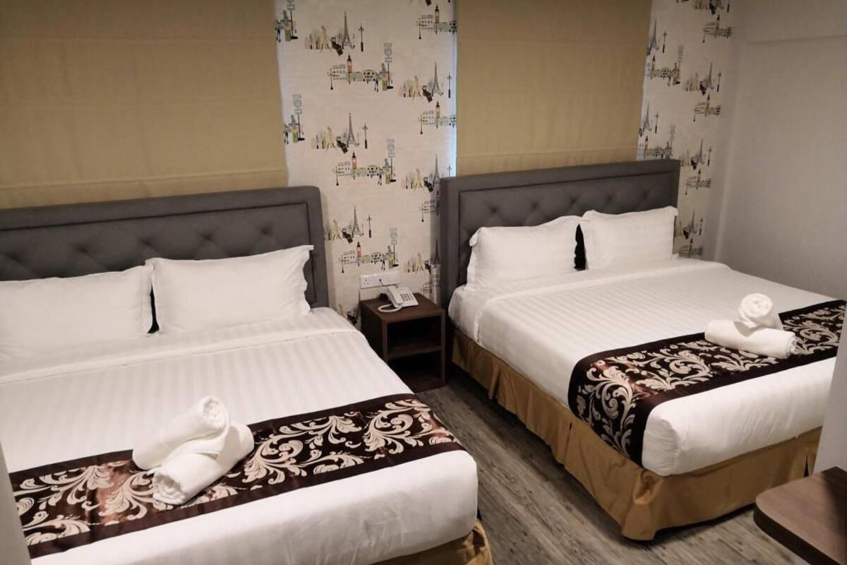 A hotel room with two beds, each with a white duvet and a brown decorative throw. There is a nightstand with a phone on it.