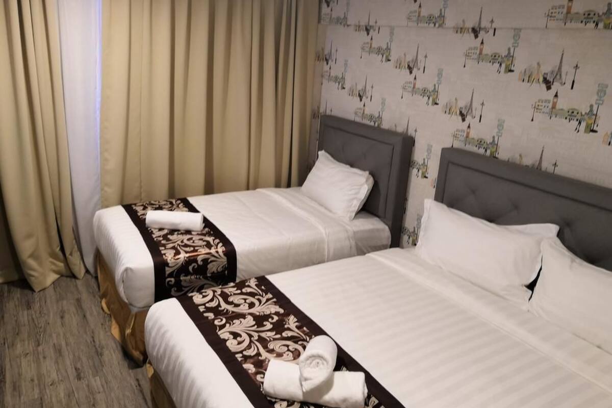 A hotel room with two beds, beige curtains, and a wall with cityscape wallpaper.