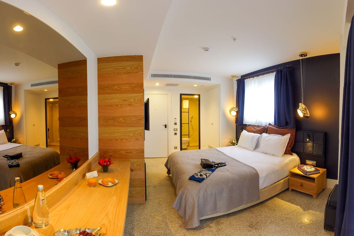 A hotel room with a bed, bedside table, mirror, and a bathroom visible through an open door.