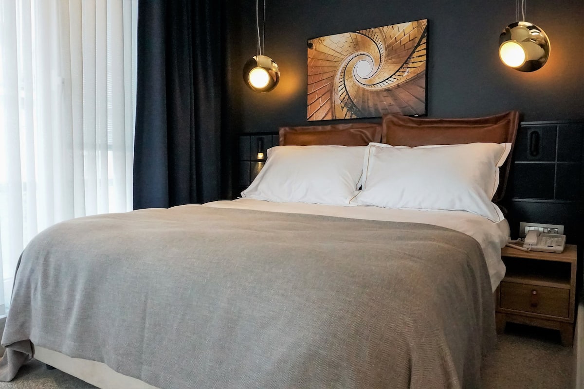 A neatly made bed with a grey blanket, a wooden headboard, and two bedside lamps.
