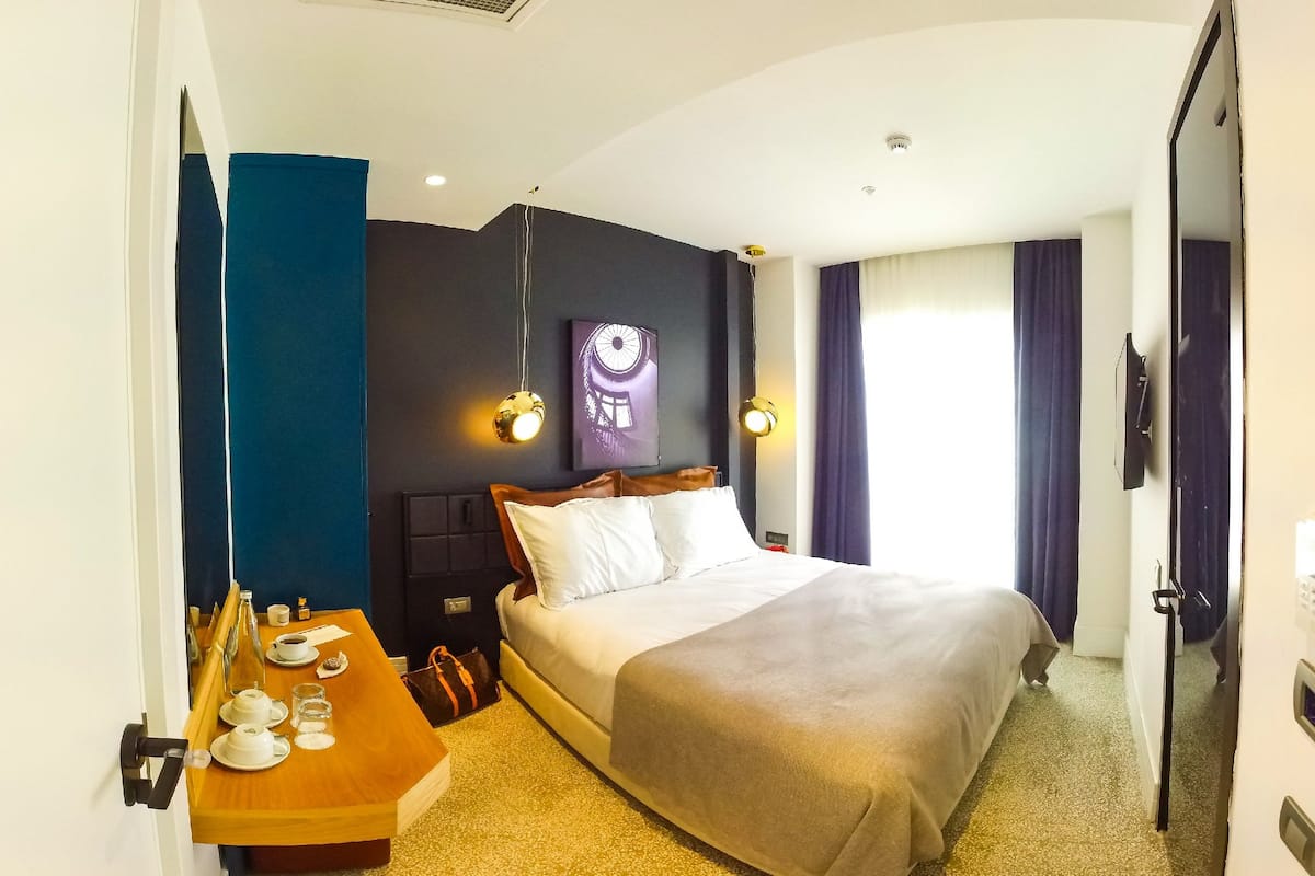 A hotel room with a bed, bedside table with tea set, and a wall-mounted TV.