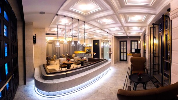 Un hall d’hôtel moderne doté d’un bar central, de plusieurs espaces de détente et d’un plafond décoratif.