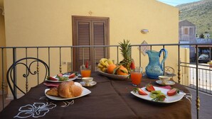 Ein Balkon mit einem Frühstückstisch, gedeckt mit Geschirr, Speisen, einer Obstschale und einer Kanne.