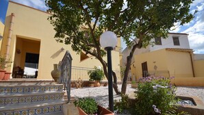 Ein Gebäude mit gelber Fassade, einer Treppe mit gemusterten Fliesen und einem Gartenbereich mit Kübelpflanzen und Blumen.