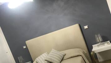 Una habitación de hotel con una cama, dos mesitas de noche, cabecera y una lámpara fijada a la pared.