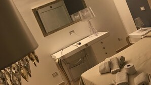 Ein Hotelzimmer mit Bett, Nachttisch, Spiegel, Waschbecken und Handtuchhalter.